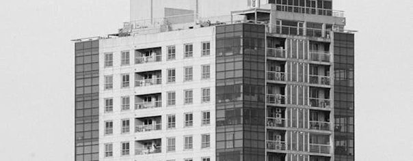 Zwart-witfoto van de gevel van een modern appartementencomplex, stedelijke woonarchitectuur met balkons en ramen.