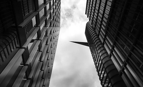 Verticaal perspectief tussen hoge gebouwen in een stadsstraat, dichte stedelijke architectuur in zwart-wit.