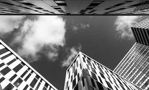 Omhoogkijkend op moderne wolkenkrabbers tegen een bewolkte hemel, geometrische stedelijke architectuur in zwart-wit.