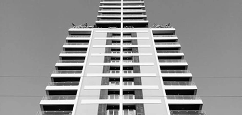 Laag perspectief van een hoge woontoren met herhalende ramen, moderne stadsarchitectuur in zwart-wit.
